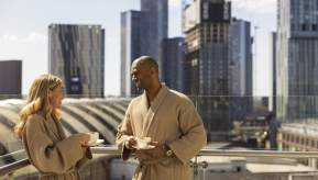 Couple on hotel balcony in dressign gowns drinking coffee with views over Manchester