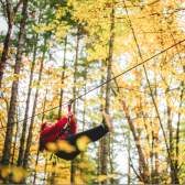 A person zip-lining through a forest with fall foliage.