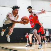 Two basketball players compete for the ball during an indoor game as one player lunges forward past a defender.