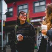 Two people walking holding coffees and chatting.