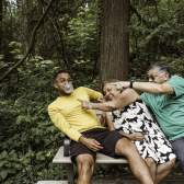A man leaning on a bench popping bubblegum with an elderly couple trying to pop the bubble.