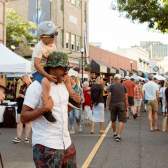 Child sitting on an adult’s shoulders at a busy outdoor street market.
