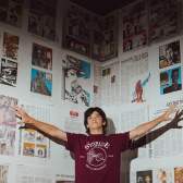 A person standing with their arms out in front of a wall covered in newspaper.