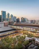 Rendering of the new Austin Convention Center building at sunset with the city skyline in the background. The image shows Waterloo Greenway creek and greenspace in the foreground