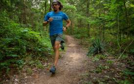 A man wearing a blue shirt and gray shorts runs on a wooded trail at Waterloo Lake Regional Park