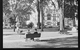black and white photograph of two people sitting on a park bench looking at the opera house