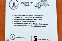 Informasjonsskilt om Markøy fyrs 300-årsjubileum, med tekst om fyrtårnets historie og tegning laget av Linn-Marita Andreassen. Skiltet er festet til en oransje murvegg.