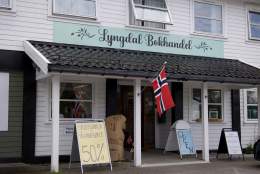 Inngangspartiet til Lyngdal Bokhandel med norsk flagg og tilbudsskilt.