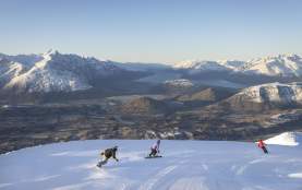 Three snowboarders riding down snowy mountain