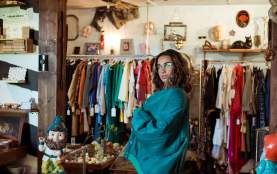 A person posing in front of a vintage store clothes rack.