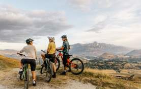 Three mountain bikers at the top of a mountain overlooking a valley with the Remarkables mountains in the background