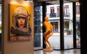 A sculpture and artwork inside a gallery with views of the street through the windows