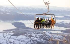 People on a chairlift at Treble Cone with snowy mountains in the background
