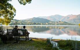 Two people sitting on a bench looking our over a lake with mountains in the background