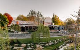 Exterior of The Woolshed Restaurant, Ayrburn with autumn coloured trees and distant mountains in the background