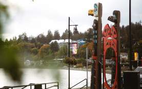 Two totem poles with a red circle gate facing the water