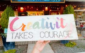 A person holding a sign reading "Creativity takes courage", outside of the Island-ish store.