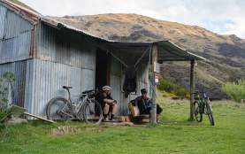 Two men taking a rest at a rugged tin back country hut with mountain bikes