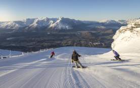 Snowboarders and skiers riding down snowy mountain