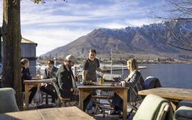 People dining outside next to the lake with the Remarkables mountain range in the background at The Boat Shed