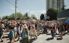 Hundreds of people take part in a Pride parade, filling a sunny Nanaimo street with rainbow colours, flags, and a celebratory atmosphere.