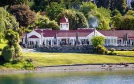 A group of people standing outside Walter Peak High Country Farm and waving to guests arriving with trees in the background and blue lake infront