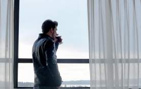 A man drinking from a glass staring out the window.