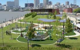 An aeriel view of the Goldring Woldenberg Riverfront Park along the Mississippi River in New Orleans' French Quarter. This shot shows the playground area with the covered performance space and city skyline in the background.