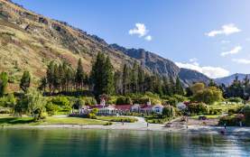 Image of Walter Peak farm house surrounded by green gardens with blue lake in the front and mountains in the background
