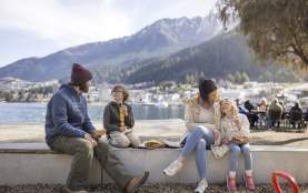 Family enjoying fish and chips by Queenstown waterfront with mountains in the background