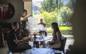 Waitress serving guests at Amisfield Restaurant, lifting up a lid of a dish with smoke coming up