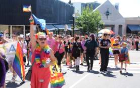 A person in rainbow and hot pink carrying a pride flag in a pride parade.