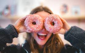 A girl holding two pink donuts up to her face, the donuts look like her eyes.