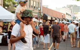 Child sitting on an adult’s shoulders at a busy outdoor street market.