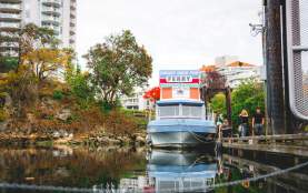 A small ferry at a dock labelled ‘Dinghy Dock Pub Ferry,’ with people boarding and reflections in the calm water.