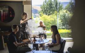 Waitress serving guests at Amisfield Restaurant, lifting up a lid of a dish with smoke coming up