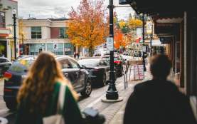 People walk along a downtown Nanaimo street with shops, parked cars, and vibrant autumn trees lining the road.
