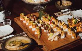 A restaurant table filled with sushi rolls, sashimi, soup, and drinks arranged on wooden boards and serving dishes.