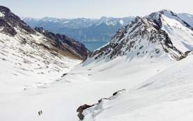 Two small figures in the distance with a wide view of Mount Larkins showing snowy mountain peaks and Lake Whakatipu