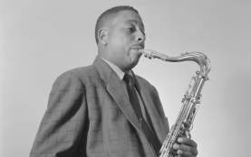 Black and white historic photo of a musician wearing a suit and a tie and playing a tenor saxophone