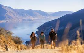 Three people walking on a steep track with mountains and lake views in the background