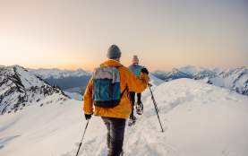Point of view image with two people snow shoeing surrounded by snow covered mountains