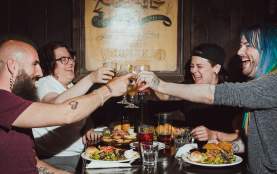 A group of four people seated at a table cheering glasses.