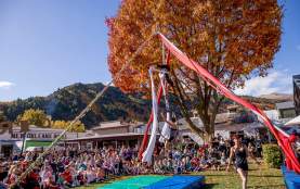 Crowd gathered around an aerial performance sounded by red and gold trees at the Arrowtown Autumn Festival