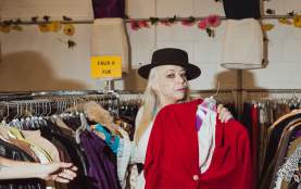 A person holding up a velvet red suit jacket at a vintage store.