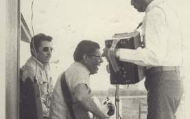 Historic photo of a small conjunto band including a guitar and an accordion player next to a building in the Montopolis neighborhood