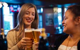 Two people cheering beers at a pub