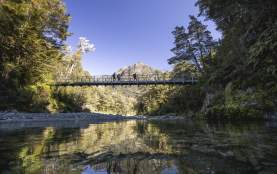 Ground of friends crossing a swing bridge on the Routeburn Track with a mountain in the background