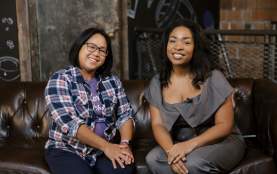 Two women smiling at the camera sitting on a couch