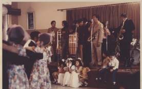 Photo of the Alfonso Ramos Band with saxophone drums bongo drum trombone and trumpet playing at the San Jose Community Center for a wedding party in South Austin around 1970